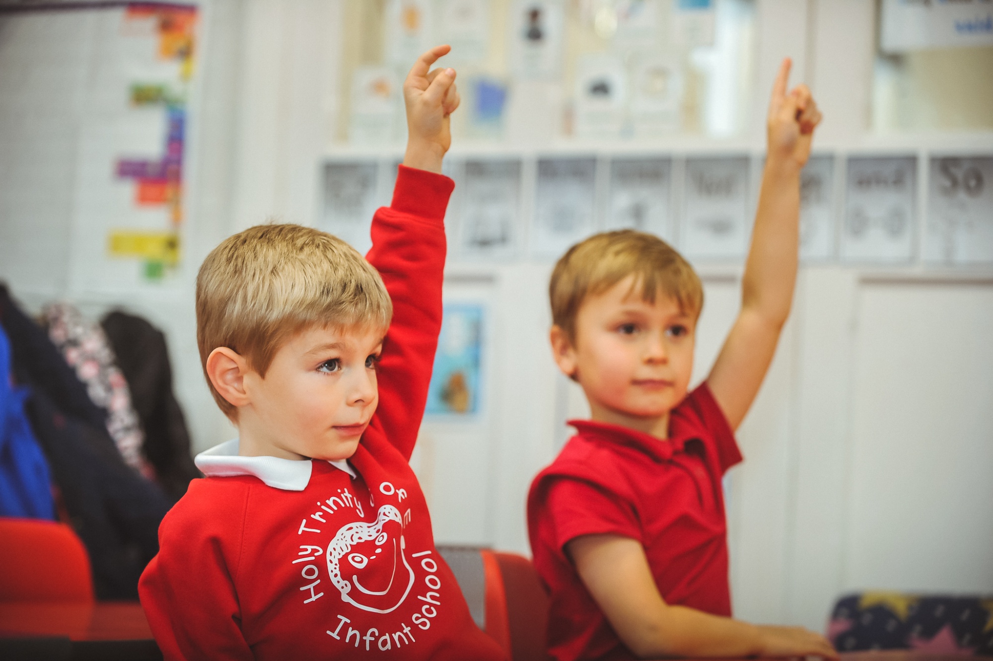 Two children in class with their hands up