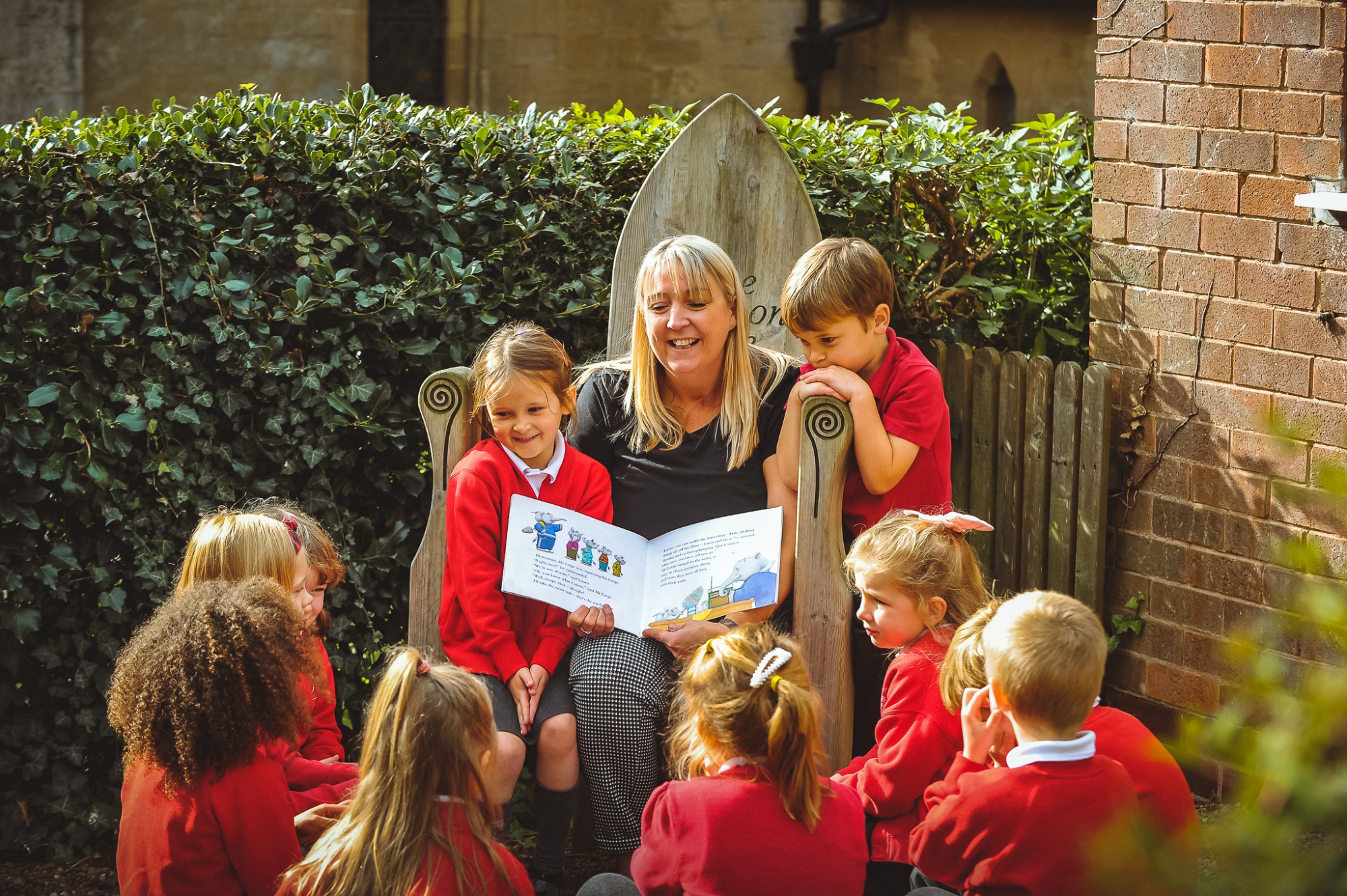 Students group reading in school garden with teacher